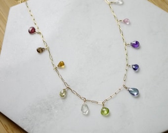 May include: A gold chain necklace with a variety of gemstone drops in different colors, including clear, pink, purple, blue, green, and brown.