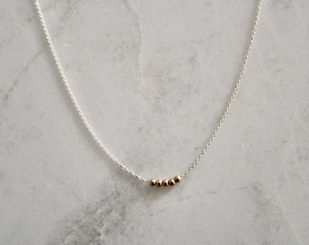 May include: A silver chain necklace with a row of five gold beads.