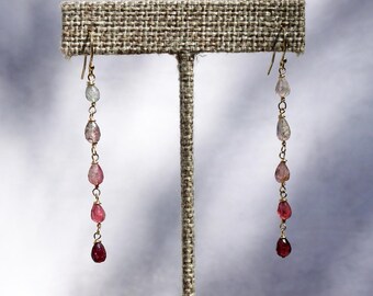 May include: A pair of long, delicate earrings with a gradient of pink and clear gemstones. The earrings are made with gold-toned metal and feature a teardrop shape.