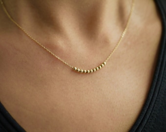 May include: A gold necklace with a delicate chain and a row of small, round beads.