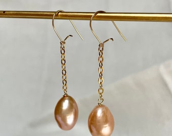May include: A pair of gold chain earrings with a pink pearl drop on each side.