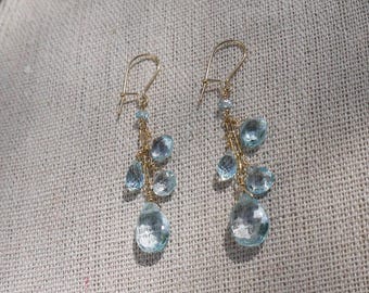 May include: A pair of gold dangle earrings with light blue teardrop-shaped gemstones. The earrings have a delicate chain design and are perfect for adding a touch of elegance to any outfit.