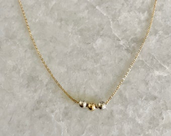 May include: A delicate gold chain necklace with three small beads, two silver and one gold.