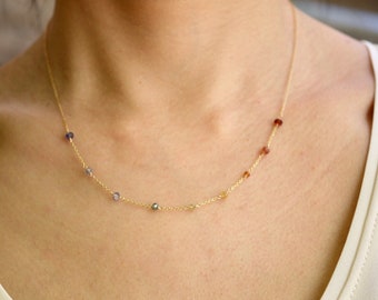 May include: A gold chain necklace with small, colorful gemstones. The necklace features a variety of colors, including purple, blue, green, and yellow.