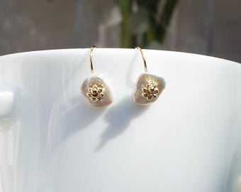 May include: A pair of gold hoop earrings with white pearl flower accents. The flower accents have a gold center with small gold beads.