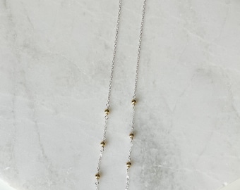May include: A pair of long silver chain earrings with small gold beads.