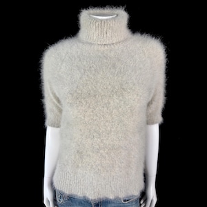 Könnte beinhalten: Ein hellgrauer, flauschiger Rollkragenpullover mit kurzen Ärmeln.