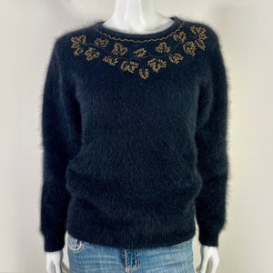 May include: A black fuzzy sweater with a gold leaf design around the neckline.