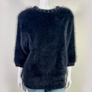 May include: A black fuzzy sweater with a beaded neckline. The sweater has a relaxed fit and is made of a soft, comfortable material.