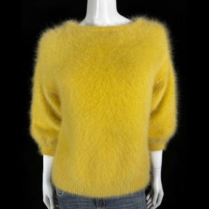 May include: A fuzzy yellow sweater with a round neckline and long sleeves.