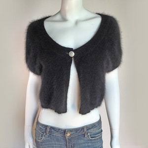May include: A black fuzzy short-sleeved cardigan with a single button closure. The cardigan is open in the front and has a scoop neckline.