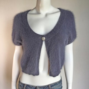 May include: A short-sleeved, gray fuzzy cardigan with a single button closure at the neckline.