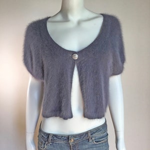 May include: A short-sleeved, gray fuzzy cardigan with a single button closure. The cardigan is cropped and has a scoop neckline.