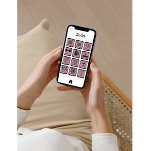 May include: A person is holding a smartphone with a pink background and a grid of icons. The icons are black and white and represent different apps. The title of the app is "Index".