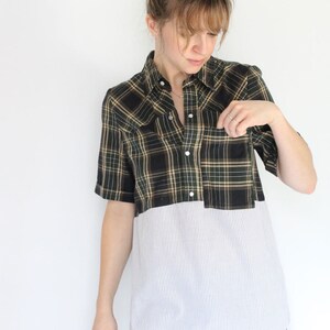 May include: A plaid and striped shirt with a button-up front and short sleeves. The shirt is a combination of black, green, and white plaid on the top half and white with thin blue stripes on the bottom half.