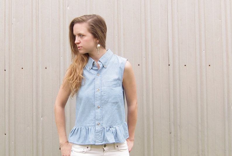May include: A light blue denim shirt with a ruffled hem and a button-up front. The shirt has short sleeves and a collared neckline.