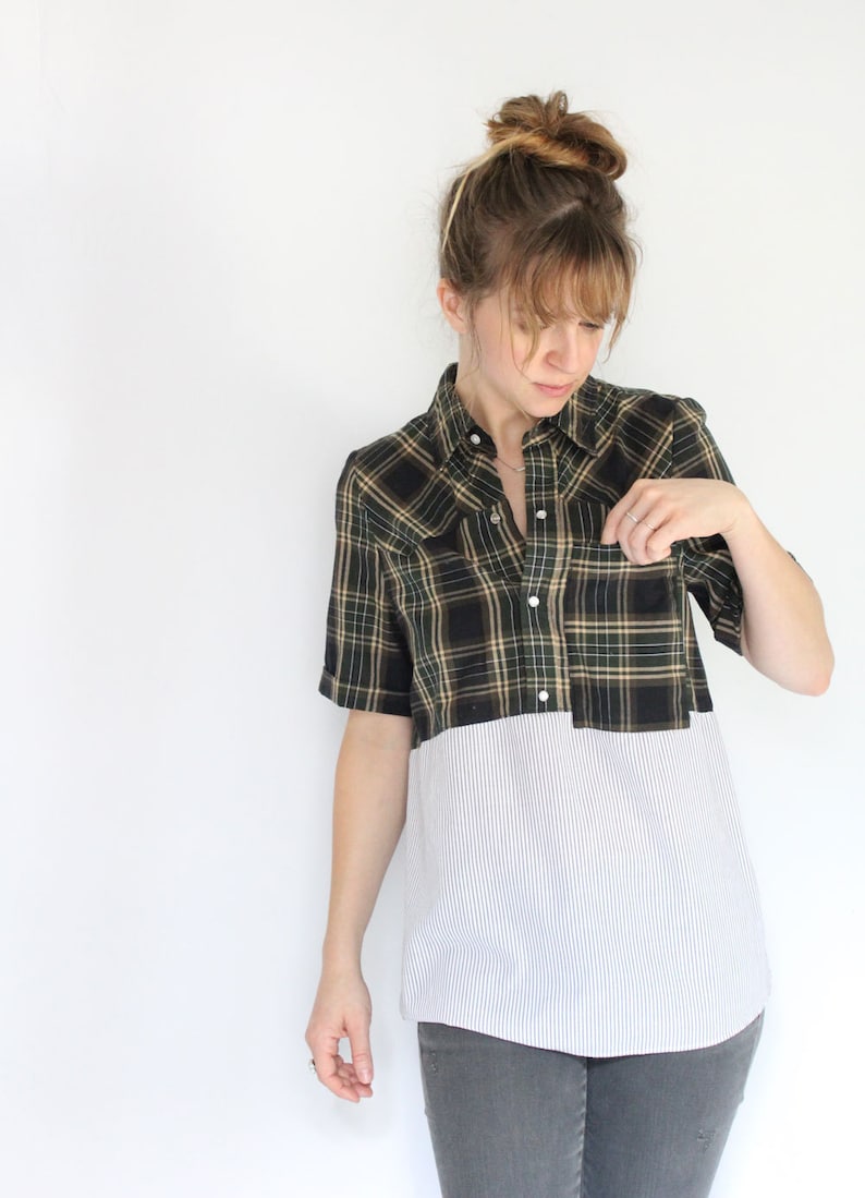 May include: A plaid and striped shirt with a button-up front and short sleeves. The shirt is a combination of black, green, and white plaid on the top half and white with thin blue stripes on the bottom half.