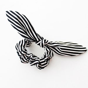 May include: Black and white striped fabric hair scrunchie with a bow. The scrunchie is made of a soft, stretchy fabric and is tied in a bow.