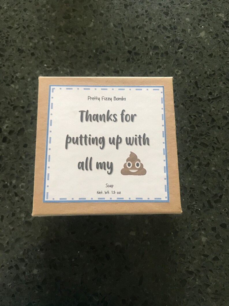 May include: A brown box with a white label that says "Pretty Fizzy Bombs" and "Thanks for putting up with all my" with a cartoon poop emoji. The label also says "Soap" and "Net. Wt. 1.2 oz".