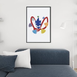 Pu&ograve; includere: Una stampa incorniciata di un design astratto in blu e rosso con un viso stilizzato e pietre preziose colorate. Il design ricorda un supereroe o un personaggio dei fumetti.