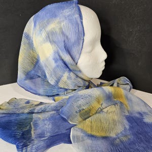 Könnte beinhalten: Ein blauer und gelber gemusterter Schal aus durchsichtigem Stoff. Der Schal ist über einen weißen Mannequin-Kopf gelegt.