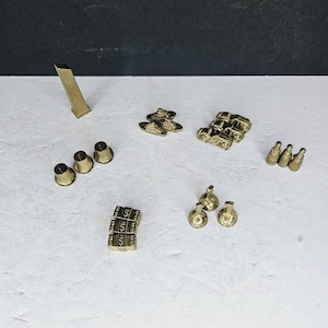 May include: A collection of small, gold-colored metal miniatures. The assortment includes a tall, rectangular piece, three thimble-shaped objects, miniature cars, ships, bottles, and stacks of what appear to be money.