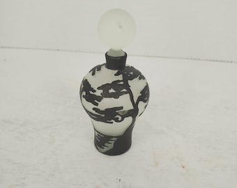 May include: A white glass bottle with a black tree design. The bottle has a frosted glass stopper.
