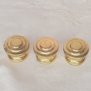 Puede incluir: Tres pomos de metal dorado con un diseño circular. Cada pomo tiene tres círculos concéntricos.