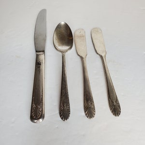 May include: A set of four silver-plated utensils, including a butter knife, a spoon, and two smaller knives. The utensils have ornate designs on the handles.