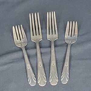 May include: Four silver forks with ornate handles. The forks are arranged in a row, with the handles pointing towards the viewer.