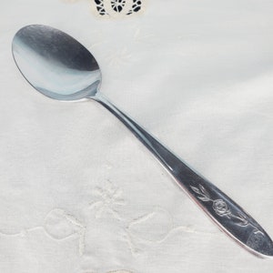 May include: A silver spoon with a rose design on the handle.