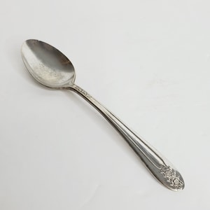 Puede incluir: Una cucharita de plata con un diseño ornamentado en el mango. La cuchara tiene un cuenco redondeado y un mango largo y delgado.