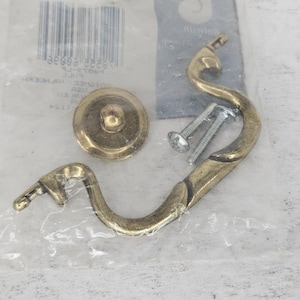 Peut inclure: Une poignée de porte décorative en or, ornée et incurvée. Elle est livrée avec deux vis pour l'installation. La poignée est emballée dans un sac en plastique transparent avec une étiquette de code-barres.