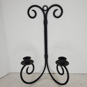 May include: Black metal wall-mounted candle holder with two candle holders and a decorative scroll design.