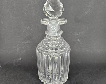 May include: A clear glass decanter with a faceted stopper. The decanter has a ribbed design and a round body.