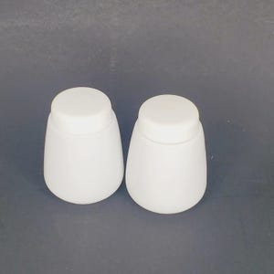 May include: Two white ceramic salt and pepper shakers with a round shape and a small hole on top.