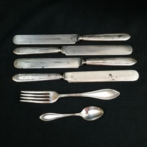 May include: A set of five silver-plated knives and a fork and spoon. The knives have ornate handles and the fork and spoon have simple designs.