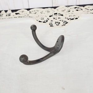 May include: A black metal double hook with rounded ends. The hook is designed for hanging items on a wall.