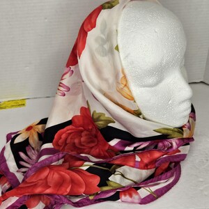 May include: A white silk scarf with a floral print of red, yellow, and purple flowers. The scarf has a black and white striped border with a purple trim.
