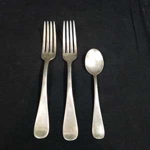 May include: Three silver utensils: two forks and a spoon. The forks have four tines each and the spoon has a rounded bowl. All three utensils have a simple, elegant design.