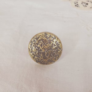 Może przedstawiać: Okrągły, złoty metalowy gałka z fakturowaną powierzchnią. Gałka ma szczegółowy wzór z wirującymi wzorami.