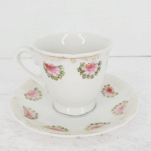 May include: A white teacup and saucer set with a pink and green floral design. The cup has a handle and a delicate floral pattern around the rim. The saucer has a matching floral pattern.