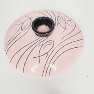May include: A pink ceramic lid with a black center hole and a stylized design of fish swimming in waves.