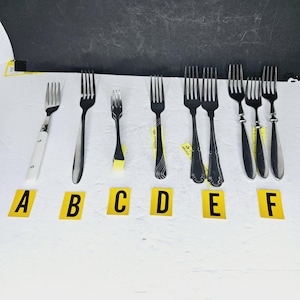 May include: Assortment of forks displayed against a white surface. The forks vary in size, style, and handle design. Some have ornate handles, while others are simple. The forks are arranged in a row, with yellow labels marked A through F.