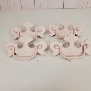 May include: Four pink metal drawer pulls with ornate designs. Each pull has a loop handle and a decorative top.