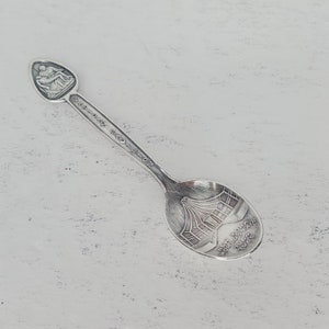 May include: Silver souvenir spoon with a depiction of the New York World's Fair 1964-1965 on the bowl and a seated figure on the handle.