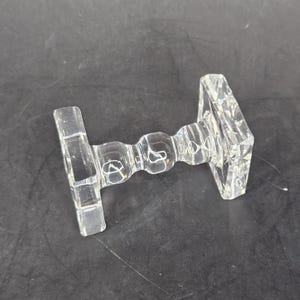 May include: A clear glass decorative stand with a square base and a round, beaded center section.