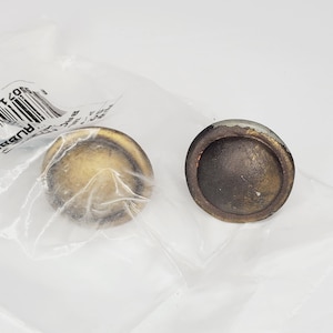 May include: Two antique gold-toned cabinet knobs with a round, slightly domed shape. The knobs have a slightly worn, distressed finish.