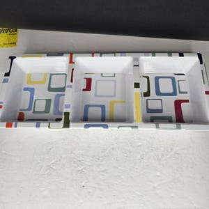 May include: A white serving tray with three square compartments. The tray has a colorful geometric pattern of squares in blue, yellow, green, and red. The tray is designed for serving snacks or appetizers.