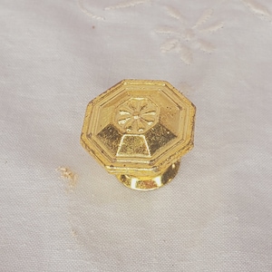 May include: A gold-toned octagonal cabinet knob with a decorative floral design in the center.
